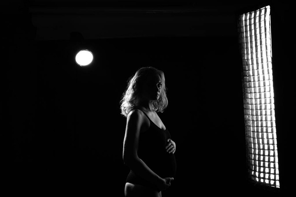 Genç ve güzel hamile bir kadın pembe arka planda duruyor. - Fotoğraf, Görsel