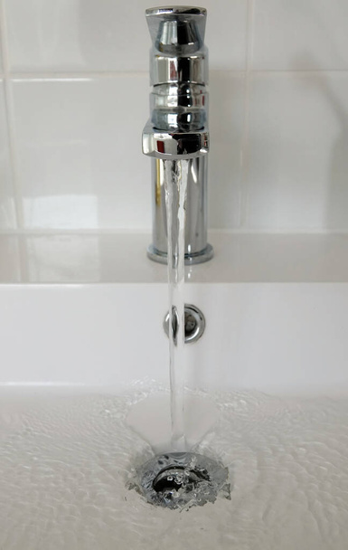 A vertical shot of a faucet on the sink with water running down and going into the drain - Foto, immagini