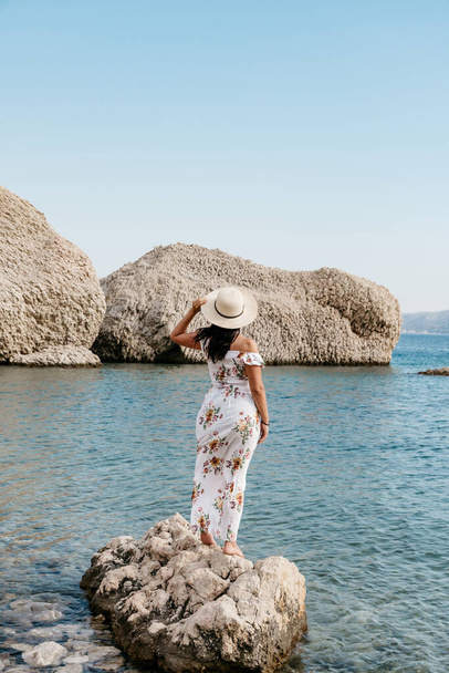 Woman in elegant long white summer dress standing on rock on beautiful Beritnica beach with large rock formations on Pag island in Croatia. - Photo, image