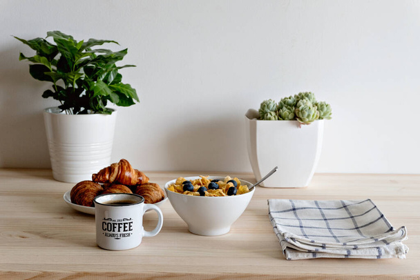 A breakfast table with coffee, croissants, and a bowl of berry cereal - Фото, зображення