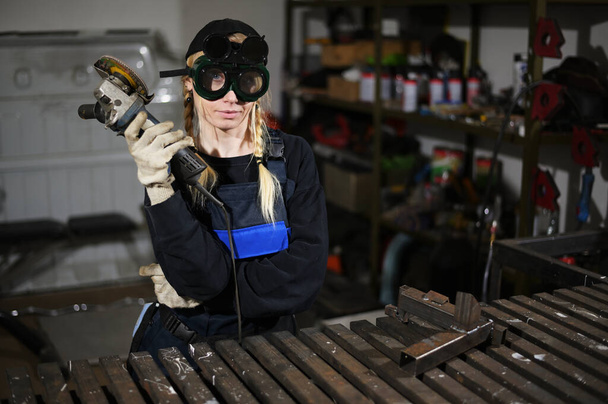 Photo of young woman with angle grinder working in protection in garage - Foto, immagini