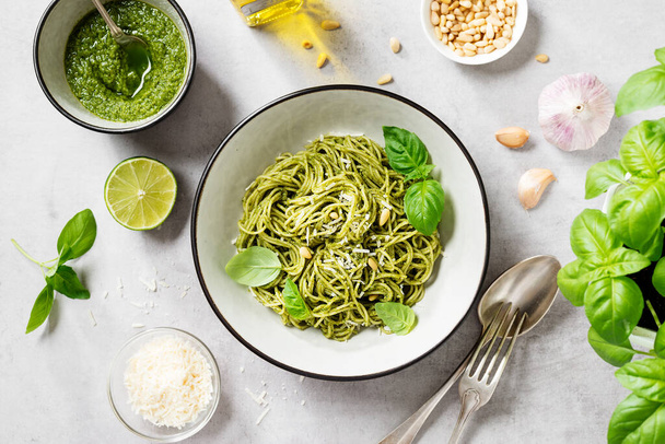 Pasta spaghetti with pesto sauce and fresh basil leaves in grey bowl. Light grey background.Top view. - Foto, immagini