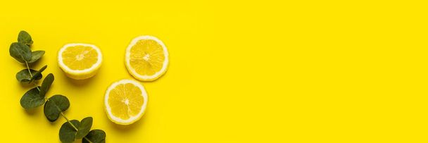 limone tagliato, spicchi di limone e un rametto di eucalipto su fondo giallo.  - Foto, immagini