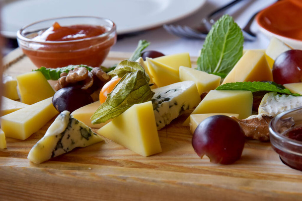 Auf einem Holzbrett eine Käseplatte, die aus mehreren Käsesorten besteht und mit Trauben dekoriert ist. Dor Blue, Pecorino Romano, Tete de Moine, Maasdam, Parmesan, - Foto, Bild