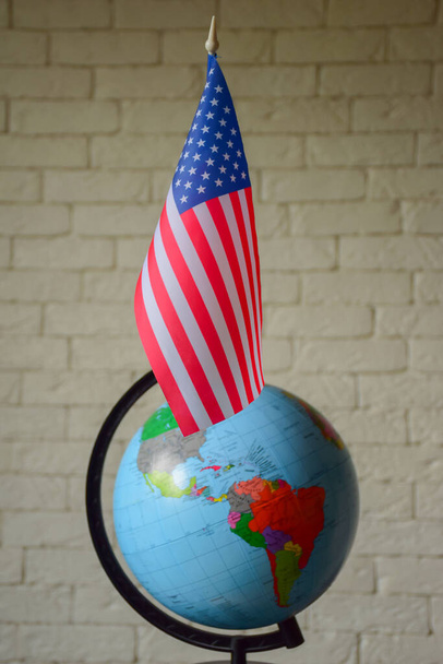 Le drapeau des États-Unis est placé contre un globe mondial flou aux contours obscurs et au mur de briques. Fond flou - Photo, image