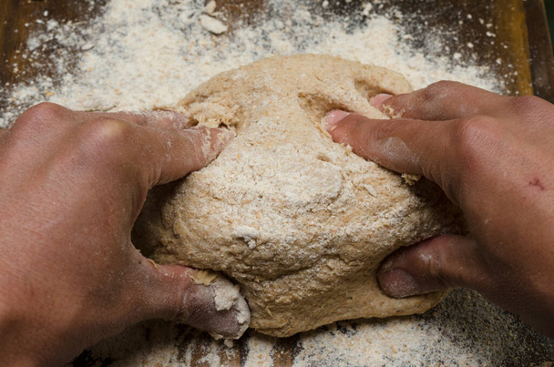 mains pétrissant un pain de blé entier sur une table de travail en bois - Photo, image