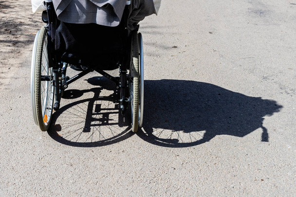 Stín invalidního vozíku a pneumatik. Stín ženy sedící na invalidním vozíku. Neviditelné ženy sedící na invalidním vozíku jsou zastíněny doprava. Vzadu na invalidním vozíku ve stínu vpravo. - Fotografie, Obrázek