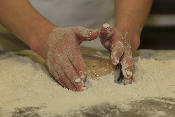 Egy nő keze gyúrja a kenyértésztát. Tésztát keresni női kezekkel a fa asztalon - Fotó, kép
