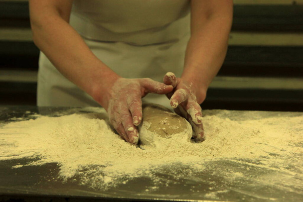 Egy nő keze gyúrja a kenyértésztát. Tésztát keresni női kezekkel a fa asztalon - Fotó, kép
