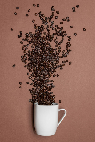色のついた背景には焙煎されたコーヒー豆が広がっています。白いカップから豆が広がっています. - 写真・画像