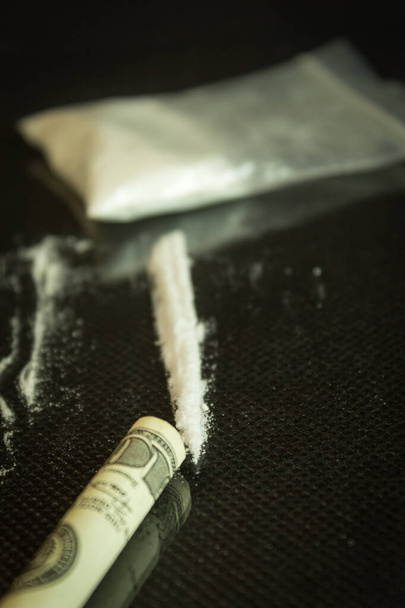 Drugs en dollars op glas, zwarte tafel. Narcotica poeder verdeeld in strepen op een gespiegelde tafel, honderd dollar buis voor drugsgebruik - Foto, afbeelding