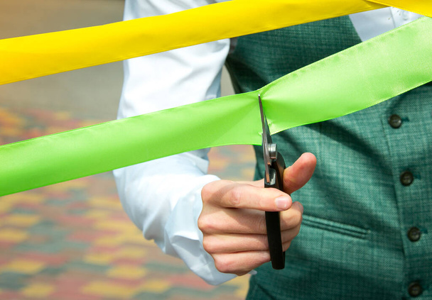 Biznesmen przecina żółte i zielone wstążki nożyczkami. Koncepcja wakacji. - Zdjęcie, obraz