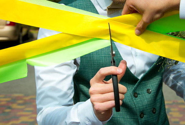 De zakenman knipt de gele en groene linten door met een schaar. Vakantie concept. - Foto, afbeelding