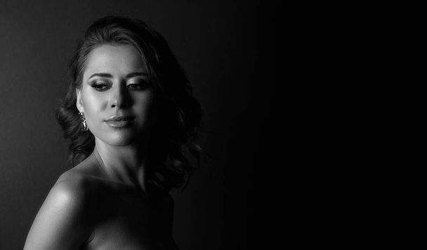 Black and white portrait of a lovely young woman posing in the shadows at studio. Empty space - Foto, Imagen
