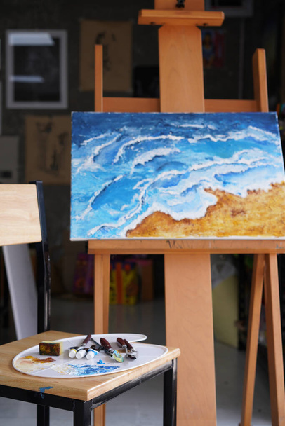 Acrylic sea and beach painting on drawing stand with palette and brush. Blue wave on golden sand hand painting with brush and knife palette technique. Art on canvas. - Photo, Image