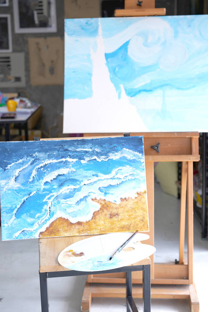 Acrylic sea and beach painting on drawing stand with palette and brush. Blue wave on golden sand hand painting with brush and knife palette technique. Art on canvas. - 写真・画像