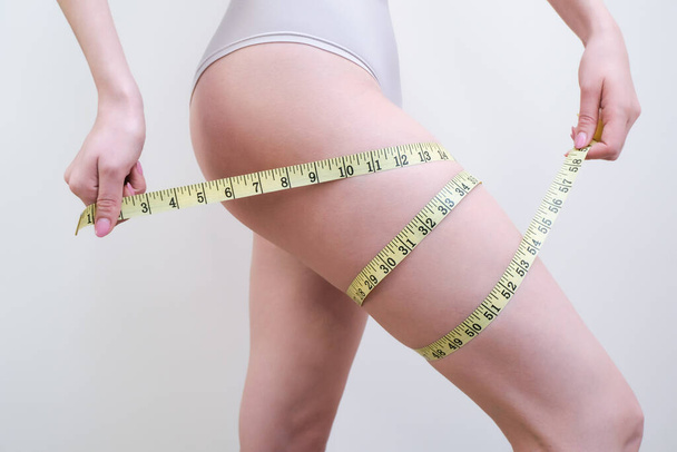 young woman is holding an a measuring tape on a light background. Cellulite problem concept - Valokuva, kuva