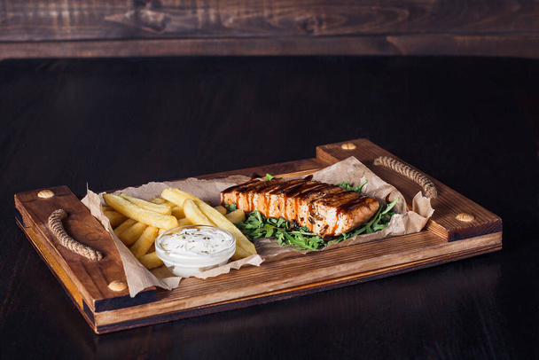 filete de salmón con papas fritas en una bandeja de madera, hermosa porción, fondo oscuro. - Foto, imagen