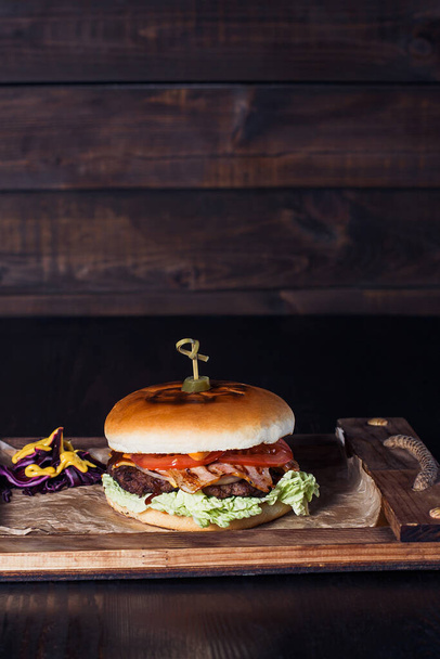 cheeseburger σε ξύλινο δίσκο σε εστιατόριο, σε σκούρο φόντο. - Φωτογραφία, εικόνα