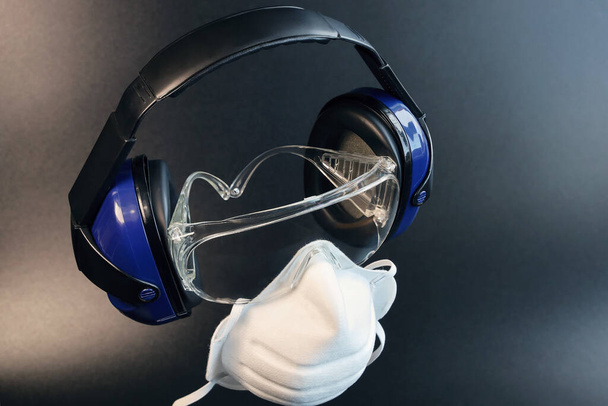 Equipamento de proteção individual, fones de ouvido e óculos com máscara filtrante respiratória, em fundo escuro com espaço de cópia - Foto, Imagem