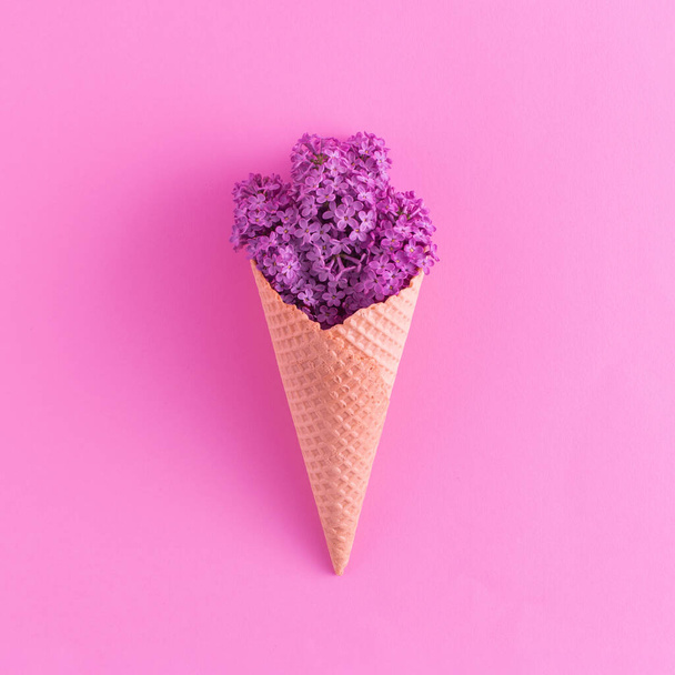 Natural ice cream cone with purple spring flowers on pastel pink background. Minimal summer flat lay composition. - Foto, Imagen