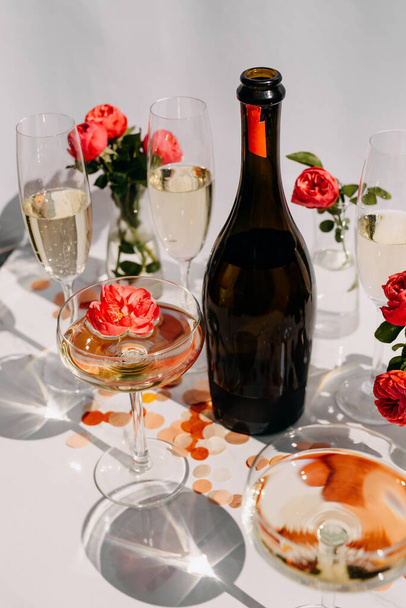 Μπουκαλάκι σαμπάνιας και γεμάτα ποτήρια με αστραφτερό κρασί σε ένα τραπέζι στο φως του ήλιου. - Φωτογραφία, εικόνα