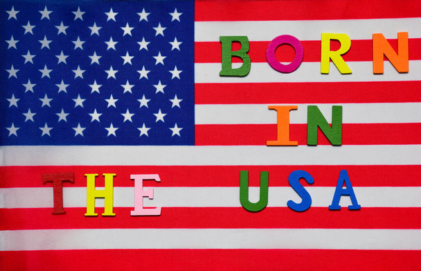 Στη σημαία των ΗΠΑ, το κείμενο που γεννήθηκε στις ΗΠΑ είναι επενδεδυμένο με πολύχρωμα διακοσμητικά γράμματα. - Φωτογραφία, εικόνα