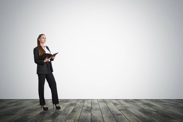 Office woman holding notebook in hands, business suit and heels. Manager on dark parquet floor reading business notes. Mockup copy space blank wall, concept of business worker - Foto, Bild