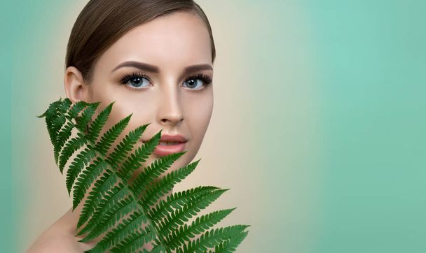 Young beautiful smiling model with natural make up, Long eyelashes and green leaf of fern. Spa, skincare and wellness. Beauty and skin care concept. - Foto, afbeelding