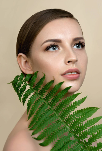 Young beautiful smiling model with natural make up, Long eyelashes and green leaf of fern. Spa, skincare and wellness. Beauty and skin care concept. - 写真・画像