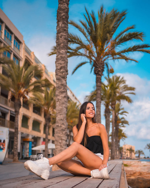 Summer lifestyle, young brunette Caucasian on the Mediterranean coast sitting on a rock by the sea in Torrevieja. Alicante, Spain - Фото, изображение