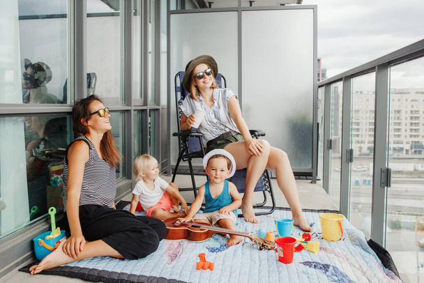 Молодые мамы проводят время с детьми на балконе дома. Пребывание во время пандемии коронавируса ковид-19 в мире. Профилактические меры против распространения вирусов. - Фото, изображение