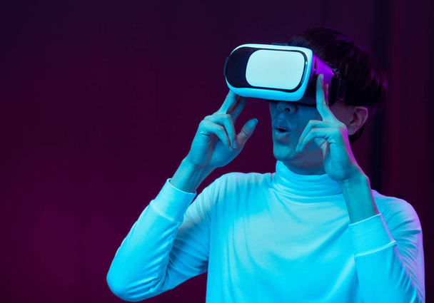 Opgewonden Aziatische jongeman draagt VR-headset in neon licht, Toekomstige technologie concept. - Foto, afbeelding