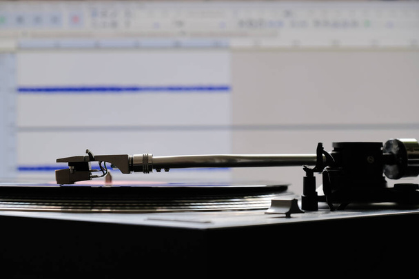 Vinyl speler cartridge en tonearm tijdens analoge naar digitale audio conversie met behulp van computer software op de achtergrond van het scherm. - Foto, afbeelding