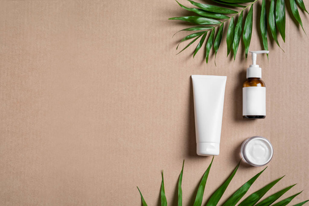 Organic cosmetic cream, body lotion and green plants on beige background, top view, copy space. Dermatology, natural skin care and spa concept with green palm leaves. - Фото, зображення