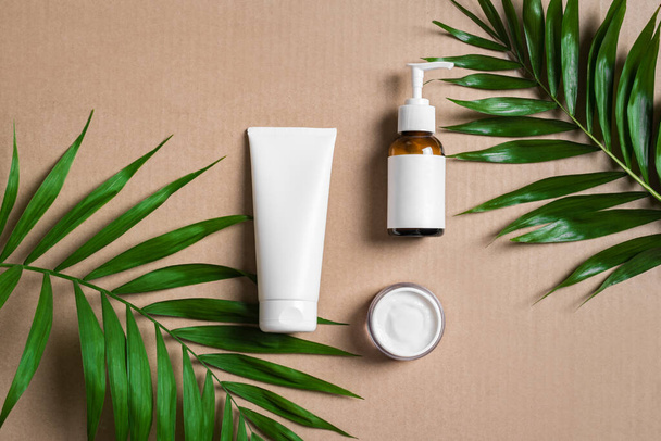 Natural cosmetic cream, body lotion and green plants on beige background, top view. Dermatology, organic skin care and spa concept with green palm leaves. - Valokuva, kuva