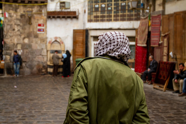 Utcai kilátás, Damaszkusz belvárosa, Szíria, ahol egy palesztin stílusú keffiyeh-t viselő férfi látható a szíriai Damaszkuszban. Cobblestone utcák és más emberek körül látható elmosódott. - Fotó, kép