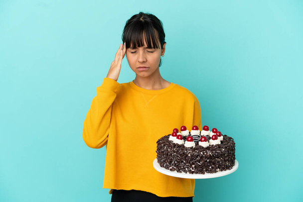 Młoda mieszana rasa kobieta gospodarstwa tort urodzinowy z bólem głowy - Zdjęcie, obraz