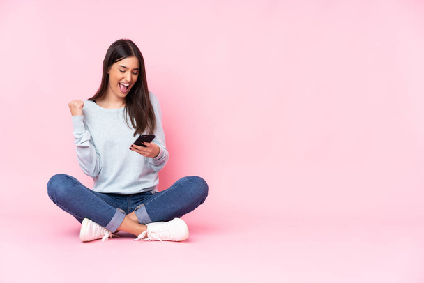 Young caucasian woman isolated on pink background with phone in victory position - Foto, Imagen