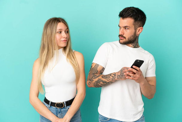 隔離された青い背景の上に若いカップル携帯電話でメッセージを読んで - 写真・画像