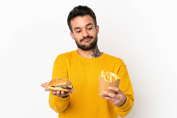 sosteniendo papas fritas y hamburguesa con queso sobre un fondo aislado - Foto, imagen