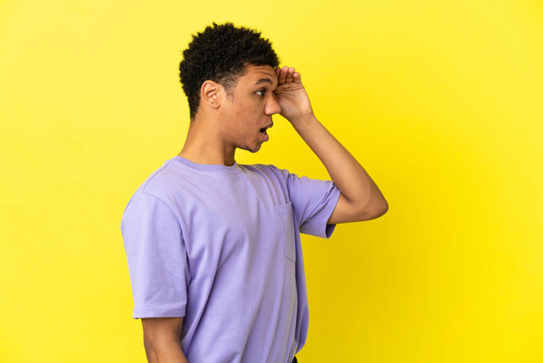 Junger afroamerikanischer Mann isoliert auf gelbem Hintergrund mit überraschendem Gesichtsausdruck, während er Seite schaut - Foto, Bild