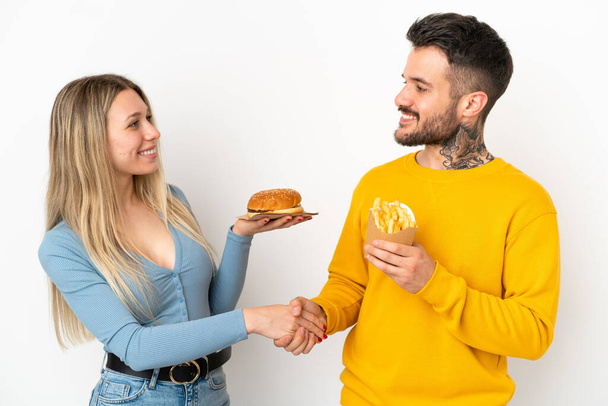 пара держит гамбургер и жареные чипсы на изолированном белом фоне рукопожатия после хорошей сделки - Фото, изображение