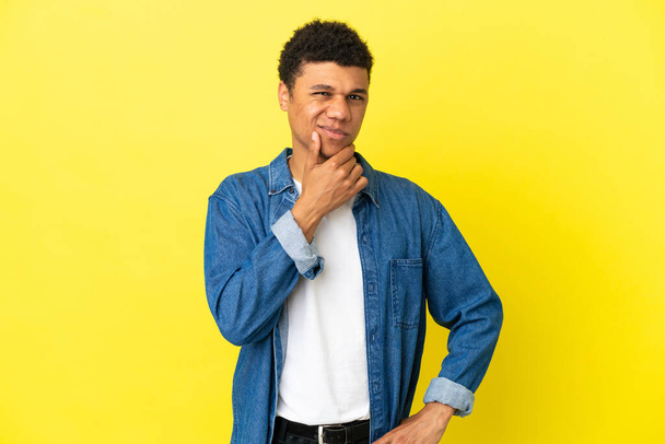 Nuori afroamerikkalainen mies eristetty keltaisella taustalla, jolla on epäilyksiä - Valokuva, kuva