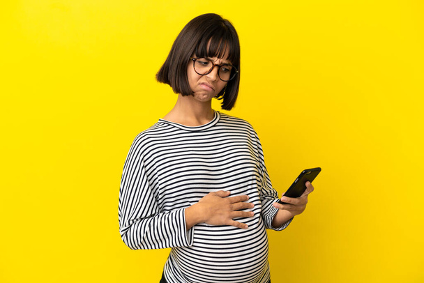 Giovane donna incinta su sfondo giallo isolato pensando e inviando un messaggio - Foto, immagini