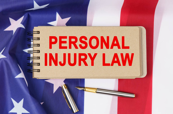Law and order concept. Against the background of the flag of the United States of America lies a notebook with the inscription - PERSONAL INJURY LAW - Foto, immagini