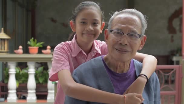 Retrato de la sonrisa adorable nieta joven tailandesa abrazo abuelo sano senior mientras posando y mirando a la cámara en casa. Juntos en familia con dos generaciones. Estilo de vida saludable. - Metraje, vídeo