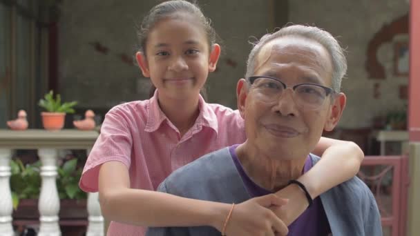 Az ázsiai imádnivaló fiatal unoka portréja boldogan öleli magához idős ősz nagyapját, miközben pózol és otthon nézi a kamerát. Két generáción át tartó együttlét a szerelemmel. Egészséges élet. - Felvétel, videó