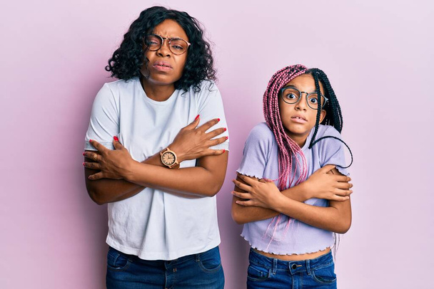 Beautiful african american mother and daughter wearing casual clothes and glasses shaking and freezing for winter cold with sad and shock expression on face  - Photo, Image