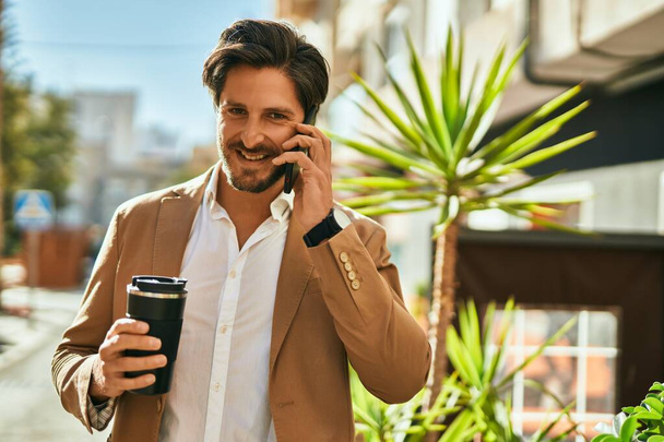 Молодой латиноамериканец разговаривает по смартфону и пьет кофе в городе. - Фото, изображение